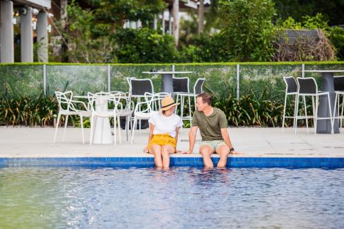 Two people sitting on the edge of a pool.